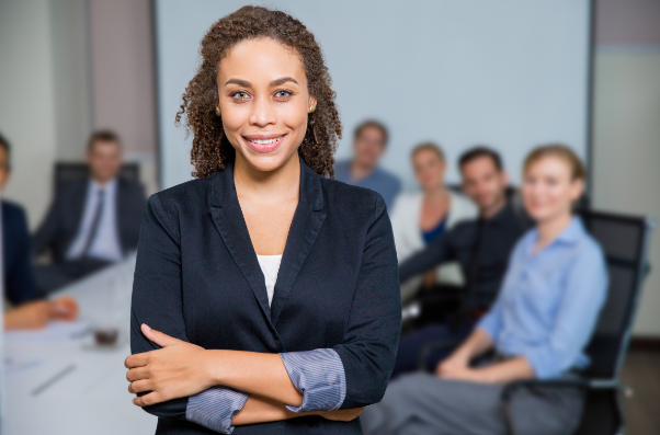 Woman professional looking at the camera with a group of people at a conference table behind her